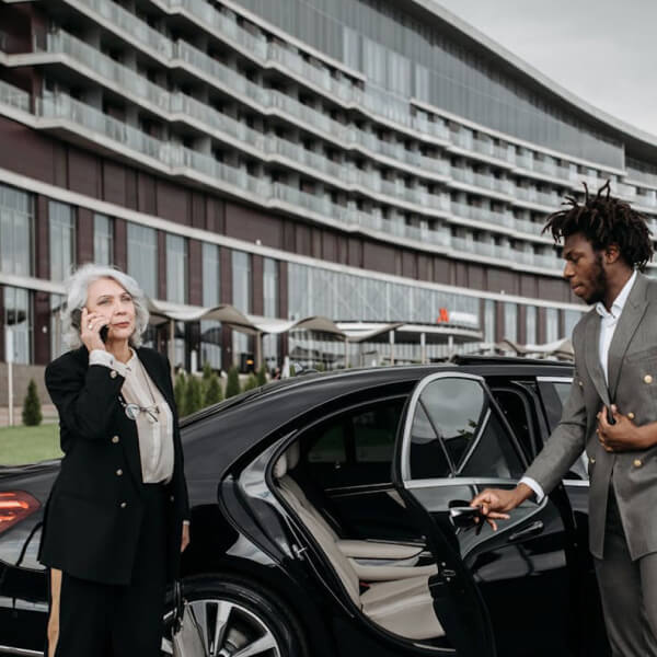 Professional chauffeur opening the door of a luxury sedan outside a hotel.